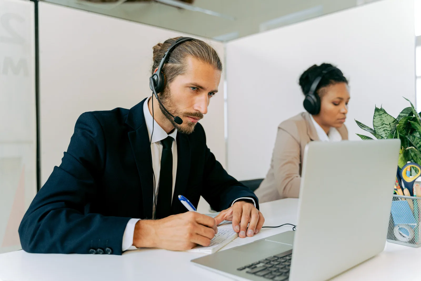 Customer service agents working together at desks, using laptops and headsets.