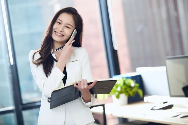Confident Asian businesswoman in white suit, smiling and talking on mobile phone in a bright office. Correcting B2B social selling measurement mistakes: preserve, repair, restate